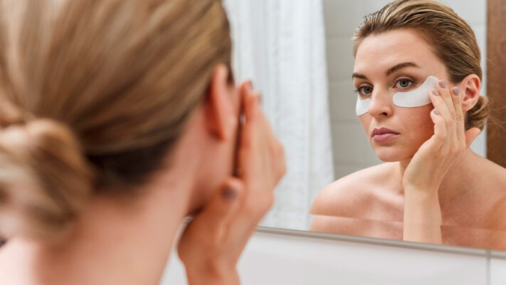 mulher se olhando no espelho com adesivos para olheiras